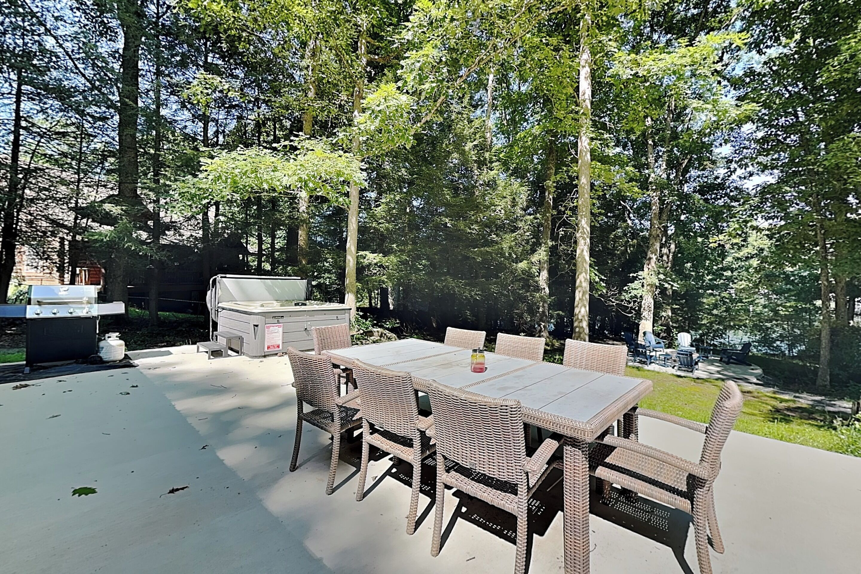 An outdoor patio with a grill, dining table, and chairs, surrounded by trees.