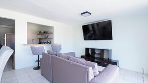 A modern living room with a sofa, a TV, and a kitchen area in the background.