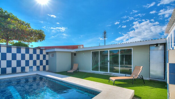 A swimming pool with two lounge chairs, a checkered wall, and a clear sky.