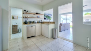 A kitchen with a dishwasher, shelves with dishes, a trash can, and a view of an outdoor patio.