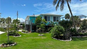 A two-story house with a green lawn, palm trees, and a small garden with rocks and plants. - The Blue Retreat in Fort Myers Beach (Fort Myers Beach)