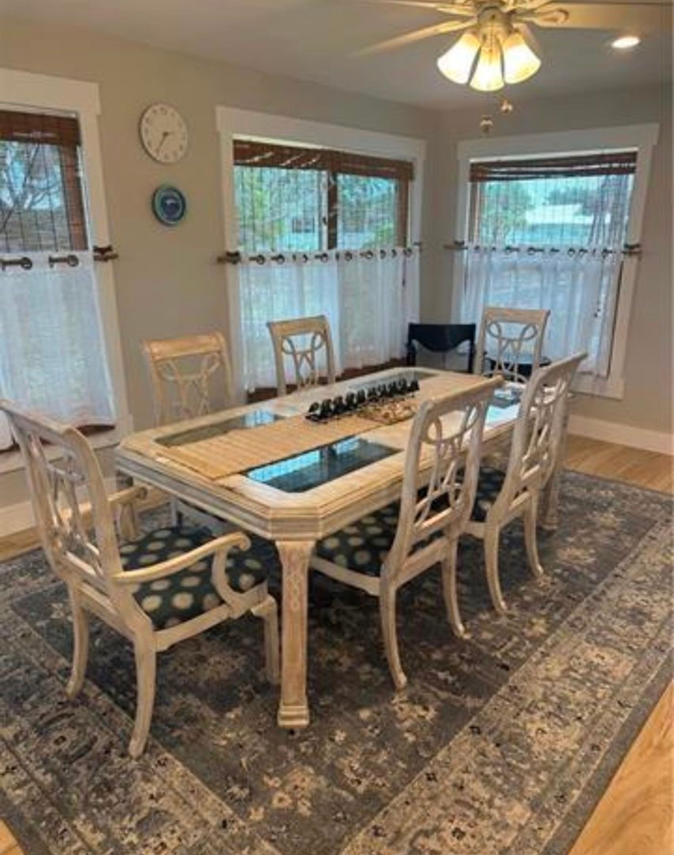 Comedor con una mesa de vidrio, seis sillas, alfombra y ventilador de techo.