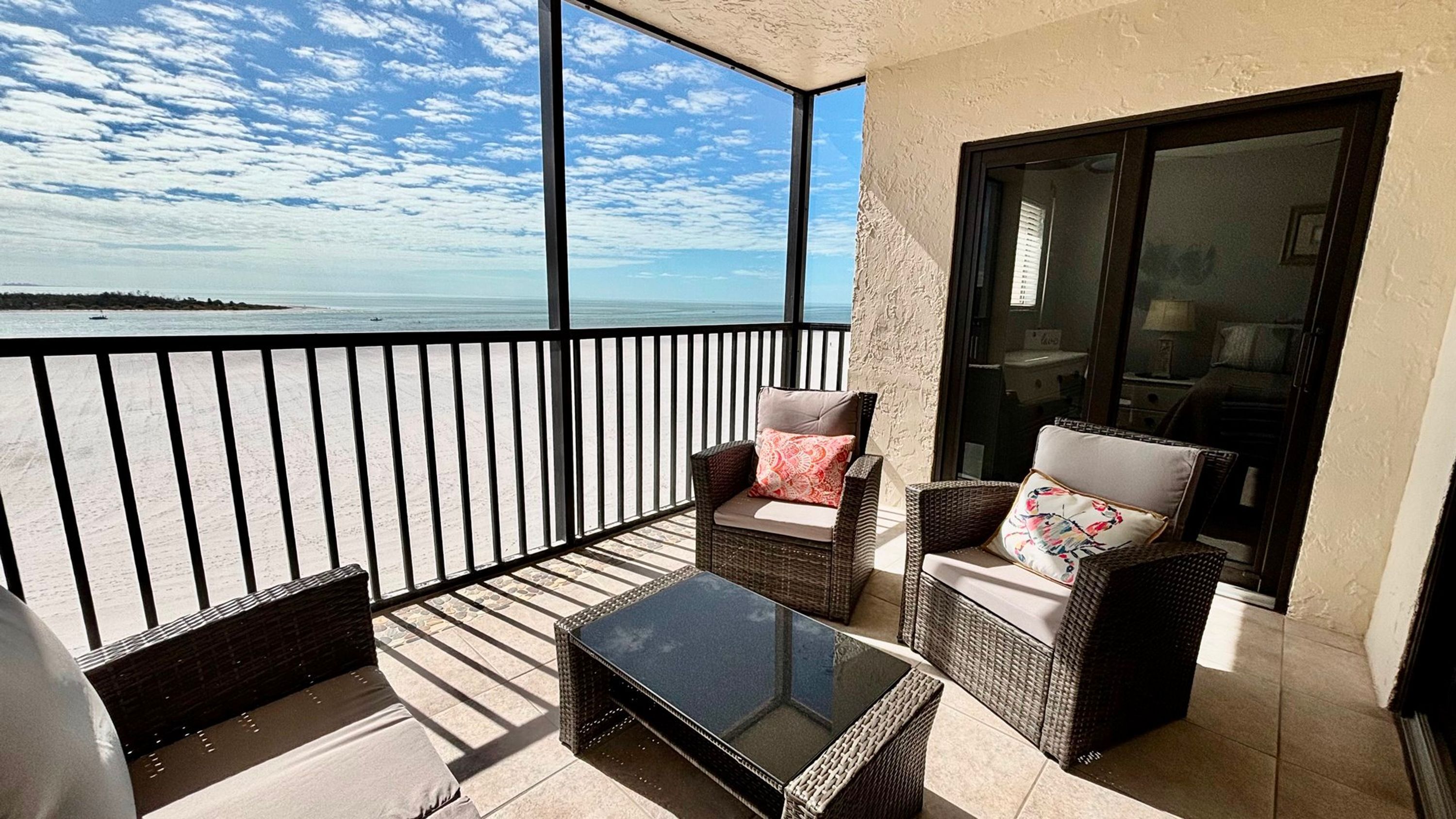 A balcony with wicker furniture, a glass table, and a view of the sea.