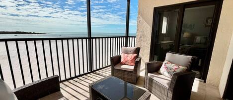 A balcony with wicker furniture, a glass table, and a view of the sea.