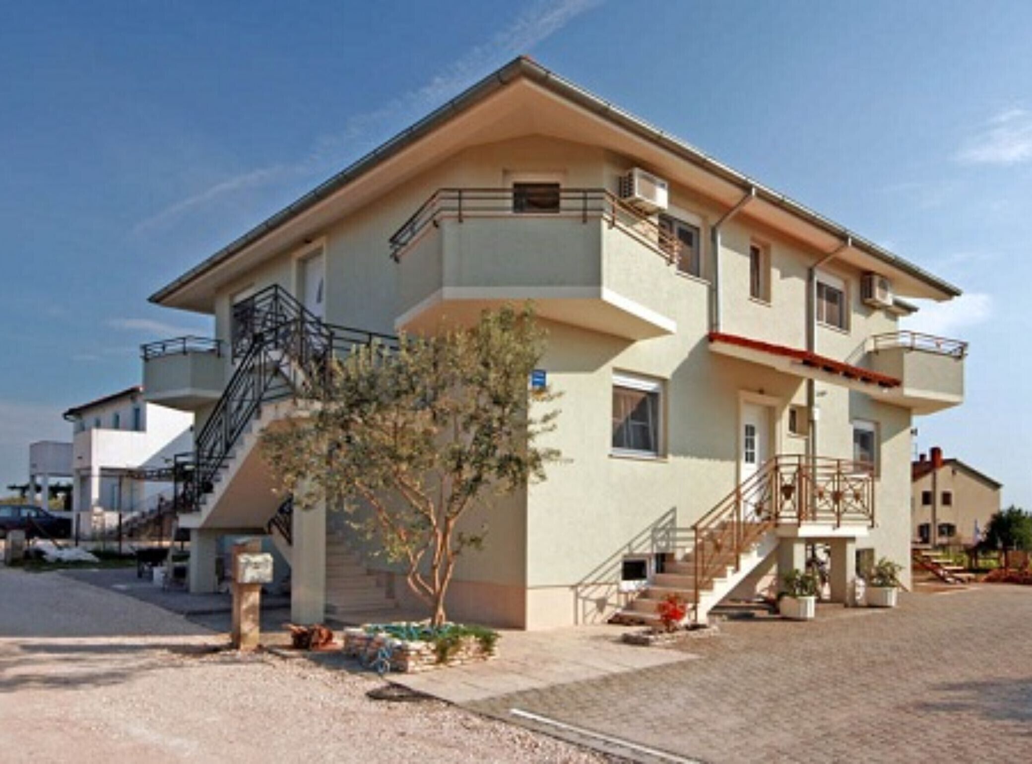 A two-story building with a flat roof, a staircase leading to the upper floor, and a small tree in the front yard.