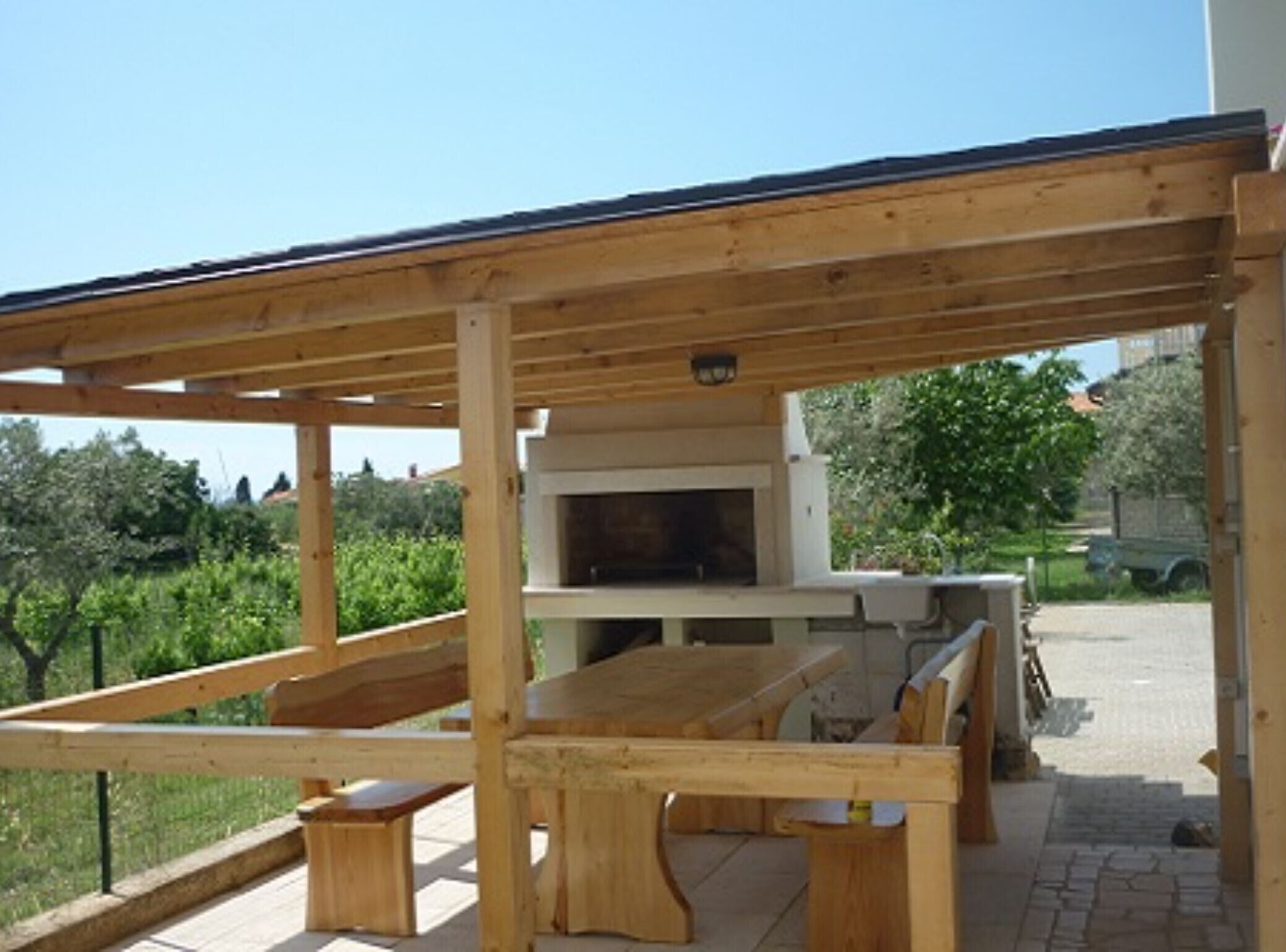 Eine hölzerne Pergola im Freien mit integriertem Grill und Sitzgelegenheit.