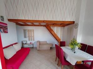 A cozy living room with a red sofa, a beige armchair, and a dining area with a table set for two. - Apartments Lighthouse - (A5) ThreeBedroom Apartment with Private Garden (Fazana)