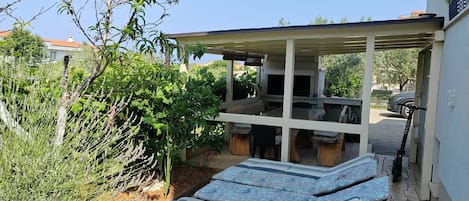 A covered outdoor seating area with a grill, a lounge chair, and a scooter.