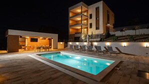 Un bâtiment moderne à deux étages doté d’une piscine, d’un espace extérieur aménagé et d’un patio bien éclairé.