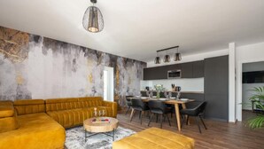 Un salon moderne comprenant un canapé d’angle, une table basse et un coin repas avec une table et des chaises en bois.