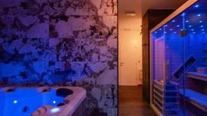 A modern bathroom with a stone wall, a bathtub with blue lighting, and a glass shower enclosure.