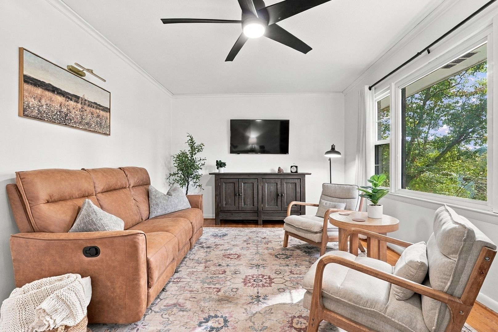 A living room with a brown sofa, a wooden chair, a small table, a cabinet, and a television on the wall.