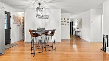 A spacious dining area with a wooden floor, a table with four chairs, and a hanging light fixture.