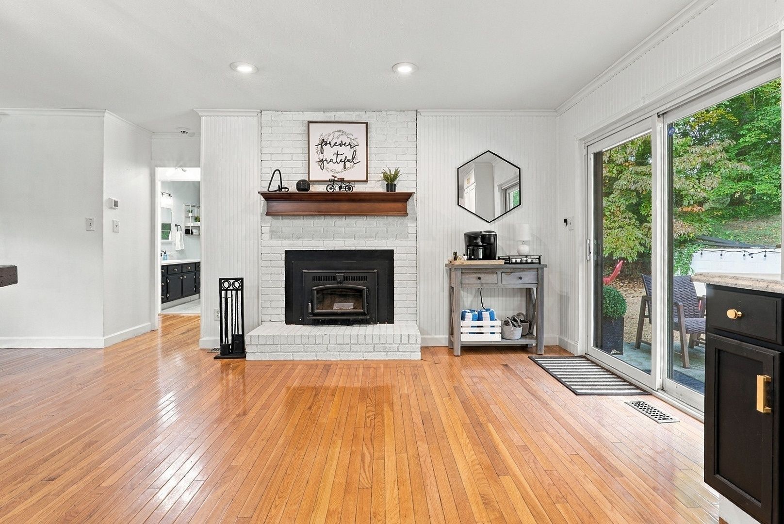 A spacious living room with a fireplace, wooden flooring, and a view of the outdoors.