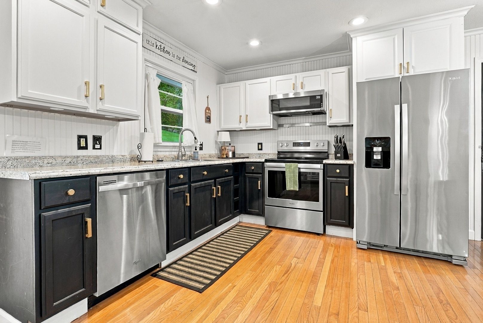 A modern kitchen with stainless steel appliances, black and white cabinetry, and a wooden floor.