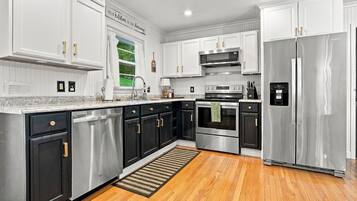 A modern kitchen with stainless steel appliances, black and white cabinetry, and a wooden floor.