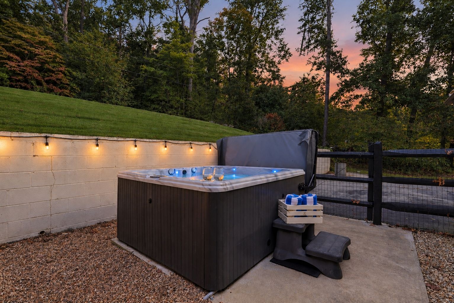 A hot tub with a wooden bench and a small table, surrounded by a concrete wall and a fence.