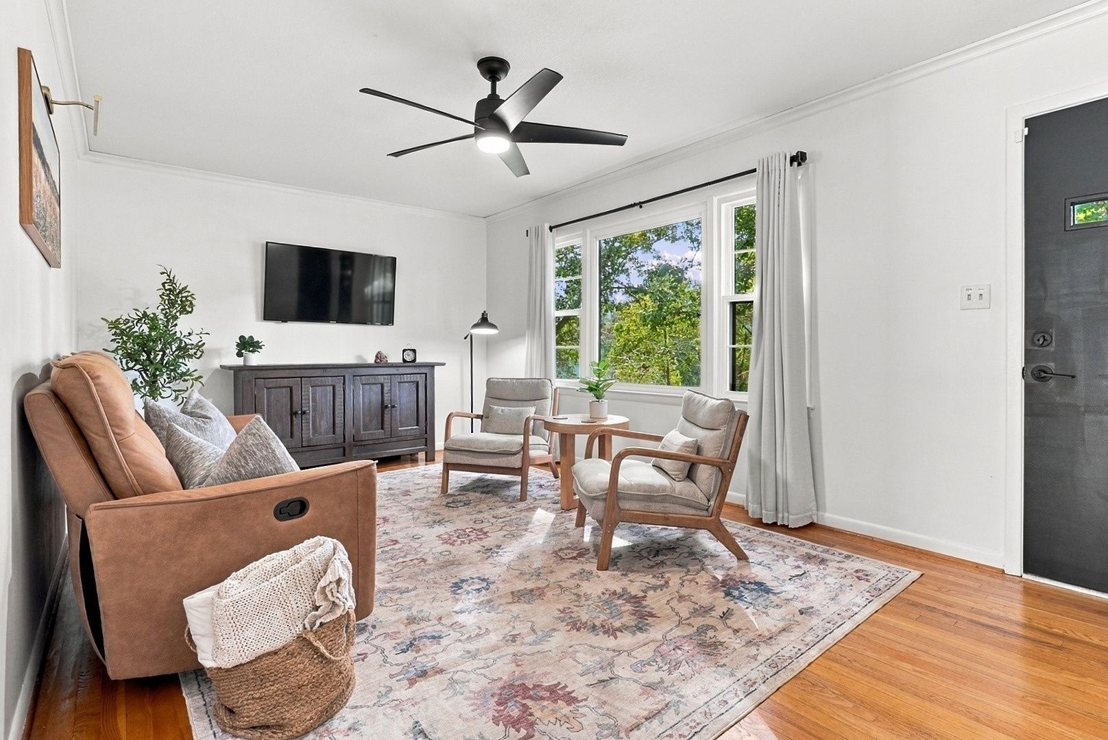 A living room with a ceiling fan, a sofa, two chairs, a TV, a cabinet, and a window with curtains.