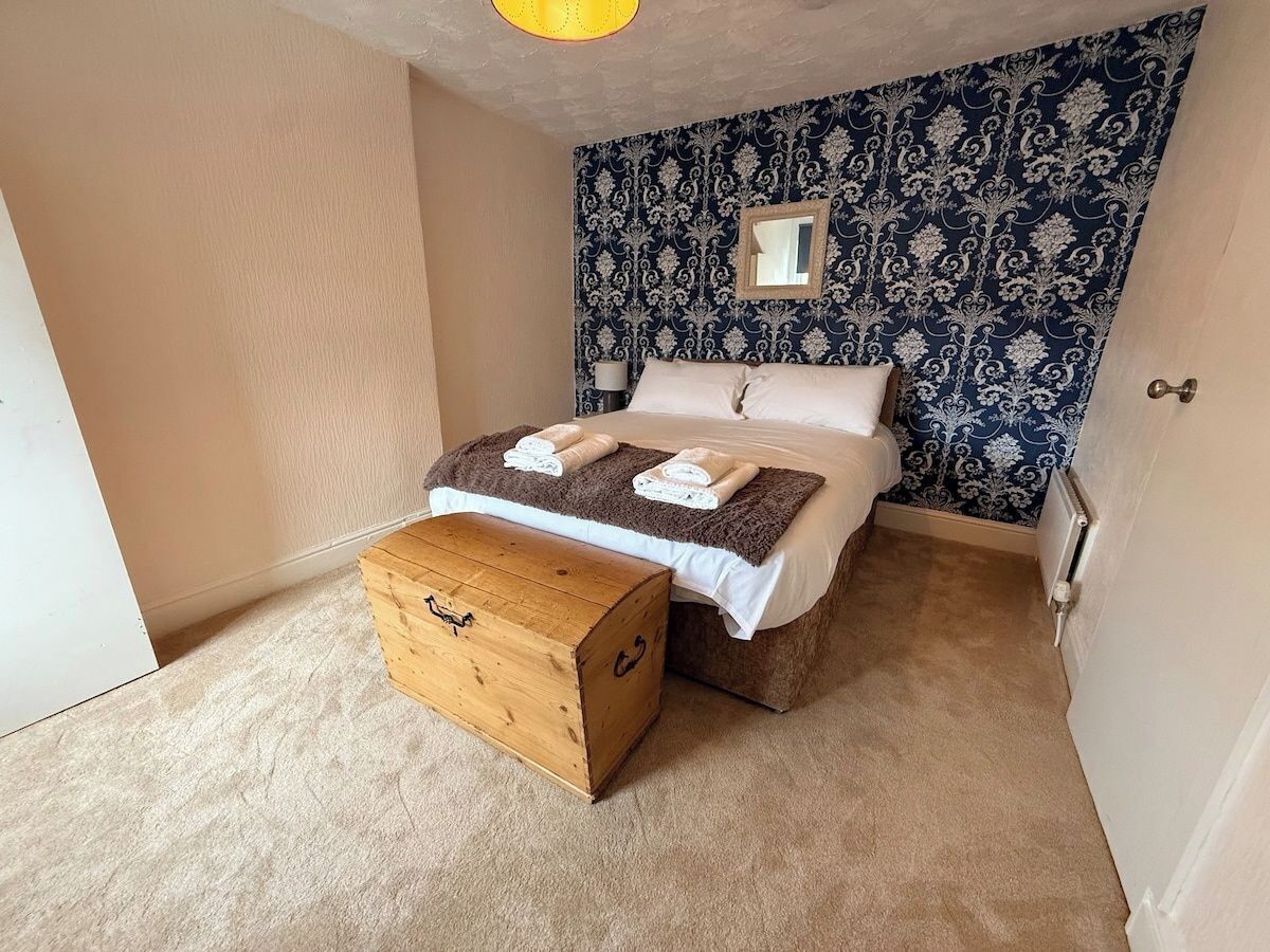 A bedroom with a bed, a wooden chest, a radiator, and a patterned wall.