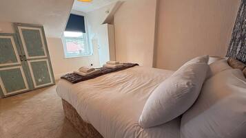 Un dormitorio con cama, almohadas, manta, ventana y puerta.