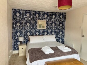A bedroom with a bed, a nightstand, a lamp, and a mirror. - Carmen Sylva 2nd Floor apartment Llandudno (Llandudno)