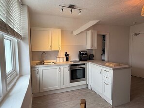 A compact kitchen with white cabinets, a built-in oven, and a coffee maker. - Carmen Sylva 2nd Floor apartment Llandudno (Llandudno)