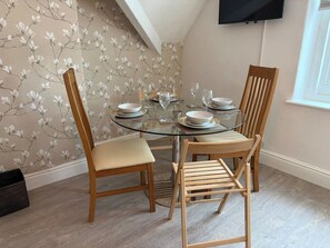 A dining area with a round glass table, wooden chairs, and a floral wallpaper. - Carmen Sylva 2nd Floor apartment Llandudno (Llandudno)
