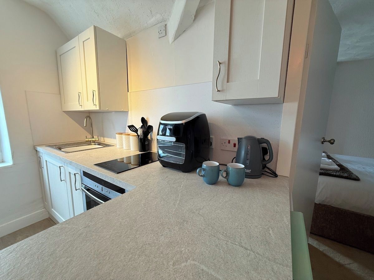 Een kleine keuken met witte kasten, een ingebouwde oven, een koffiezetapparaat en twee mokken op het aanrecht.