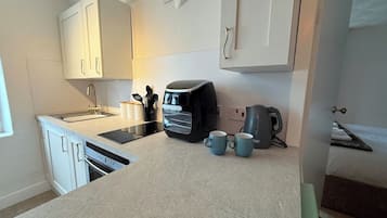 Een kleine keuken met witte kasten, een ingebouwde oven, een koffiezetapparaat en twee mokken op het aanrecht.