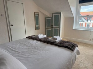 Ein Schlafzimmer mit Bett, Fenster, Tür und Spiegel.