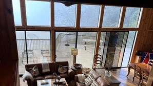 Amplia sala de estar con ventanas grandes, piso de madera y una zona de estar acogedora con una mesa de centro y cojines.