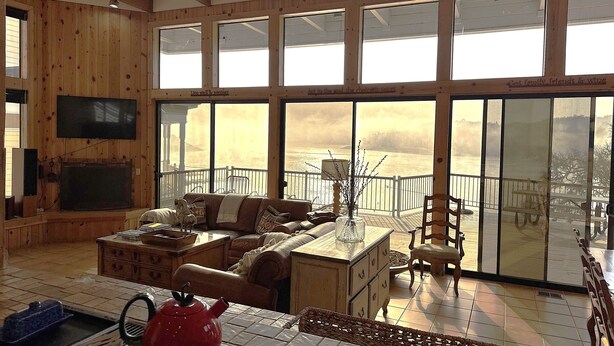 Un salón amplio con un televisor grande, asientos cómodos y una vista panorámica a través de grandes ventanales.