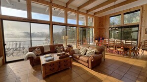 Un salón amplio con ventanas grandes, techo de madera y vista al lago.