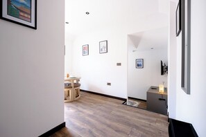 A hallway with wooden flooring, a round table with chairs, and framed artwork on the walls. - James Court Llandudno Luxury Apartment 2 & Parking (Llandudno)