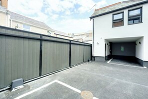 A parking area with a gated entrance, a building with a white facade, and a clear sky. - James Court Llandudno Luxury Apartment 3 & Parking (Llandudno)