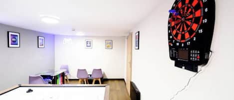A dartboard mounted on a wall, a pool table, and a seating area with chairs.