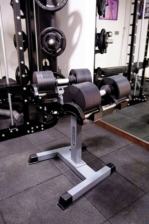 Eine Gewichtbank mit verstellbaren Hanteln und einem Squat-Gestell in einem Fitnessstudio.