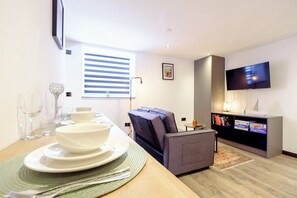 A modern living room with a dining area, a flat-screen TV mounted on the wall, and a sofa. - James Court Llandudno Luxury Apartment 3 & Parking (Llandudno)