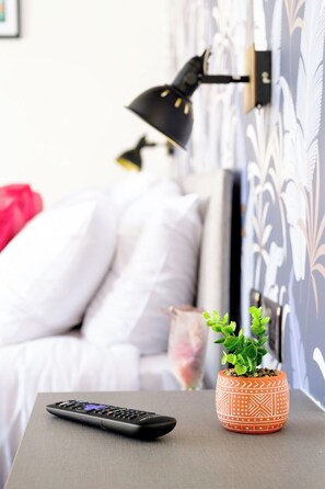 A bed with white bedding, a black lamp, a remote control, and a potted plant on a bedside table. - James Court Llandudno Luxury Apartment 6 & Parking (Llandudno)
