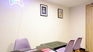 Ein Zimmer mit einem leuchtenden Neon-Gamecontroller, einem Tisch mit Stühlen und zwei gerahmten Bildern an der Wand.