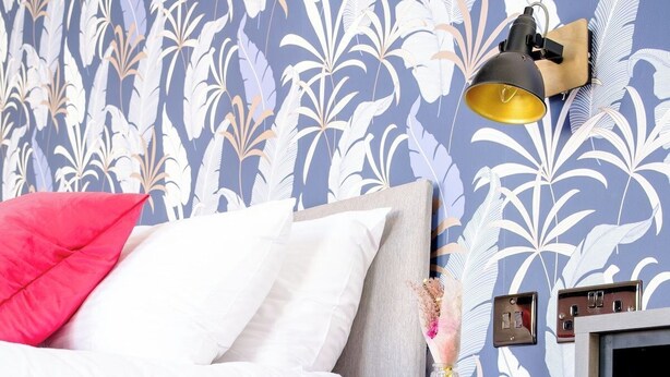 Ein Schlafzimmer mit einem Bett, einem Nachttisch, einer Lampe und einer Wand mit Blumenmuster.