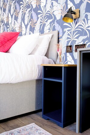 A bedroom with a bed, a nightstand, a lamp, and a wall with a floral pattern. - James Court Llandudno Luxury Apartment 6 & Parking (Llandudno)