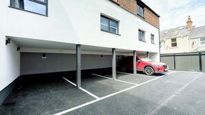 Ein Parkplatz mit einem roten Auto, einem weißen Gebäude und mehreren Fenstern.