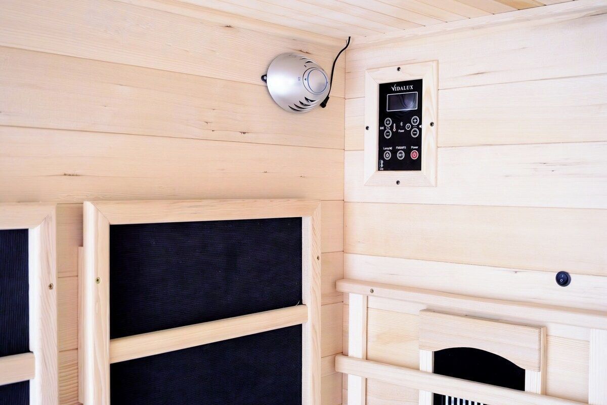 A sauna room with a control panel, wooden benches, and a ceiling vent.