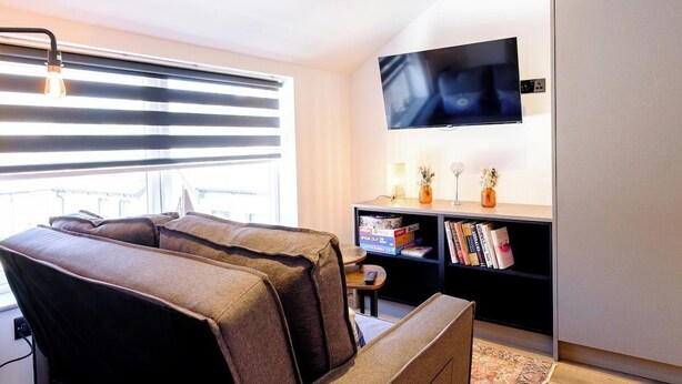 Ein modernes Wohnzimmer mit einer Couch, einem flachbildfernseher an der Wand und einem Bücherregal.