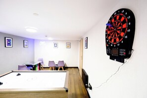En pilkastavla som hänger på väggen, ett biljardbord och en sittgrupp med stolar.