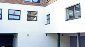 Ein mehrstöckiges Gebäude mit weißer Fassade, zahlreichen Fenstern und einem sichtbaren Backsteinbereich im oberen Geschoss.