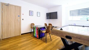 Ein Zimmer mit Holztür, einem Tisch mit Stühlen, einem Flachbildfernseher und einem Fenster mit Jalousien.