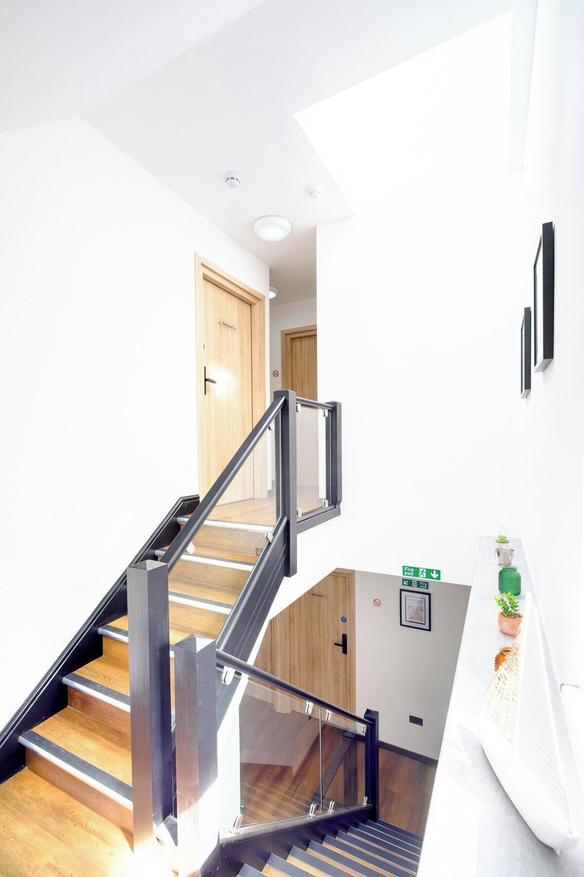 Un escalier moderne avec des rampes en verre, un revêtement de sol en bois et un panneau indiquant la sortie de secours en cas d’incendie.