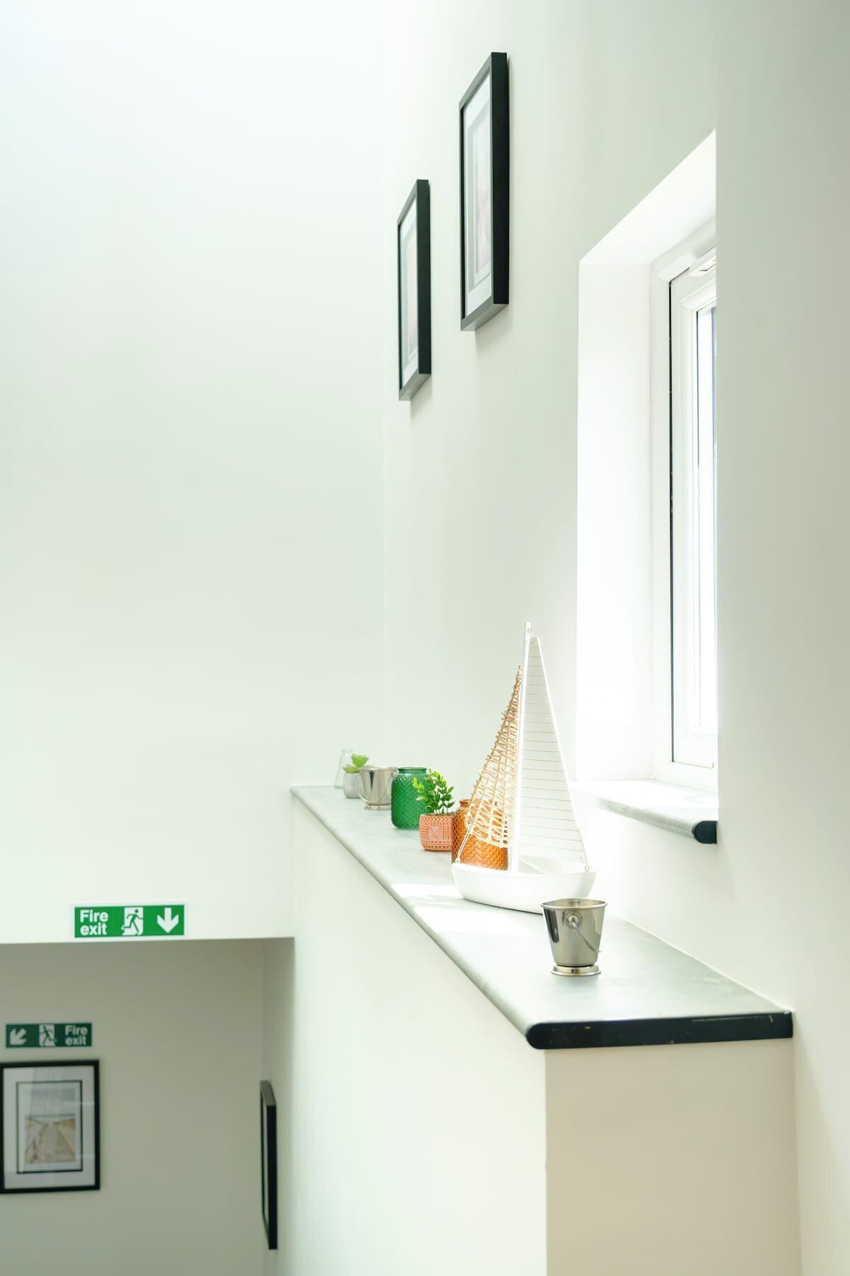 A corridor with a white wall, a window, and a fire exit sign.